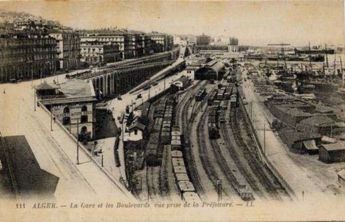 A droite, la voie principale des C.F.R.A. entre la gare et le quai. A gauche, sur le boulevard le kiosque ·Waïsse· 